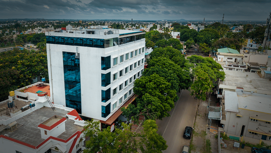 Daytime aerial view of the hotel building with surrounding trees, roads and neighbouring buildings.