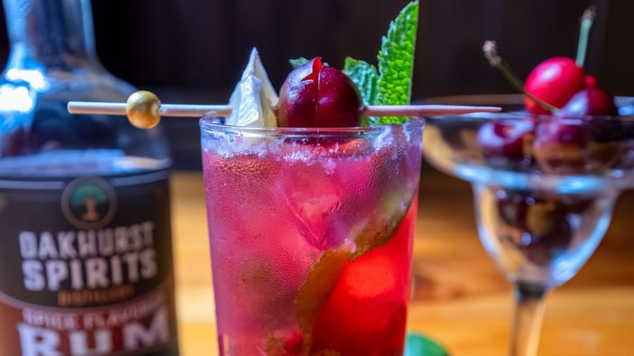 Bright red rum cocktail with mint, cherry, and lime beside a bottle of Backwards Spirits at Narrow Gauge Inn.