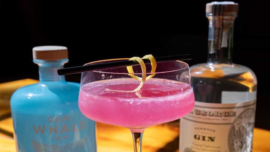 Two vibrant cocktails with lemons and gin bottles on a wooden bar under warm lighting at Narrow Gauge Inn.
