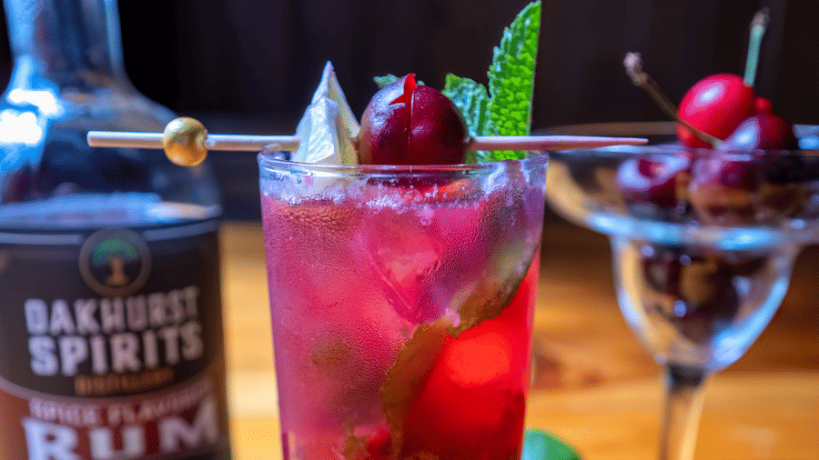 Bright red rum cocktail with mint, cherry, and lime beside a bottle of Backwards Spirits at Narrow Gauge Inn.