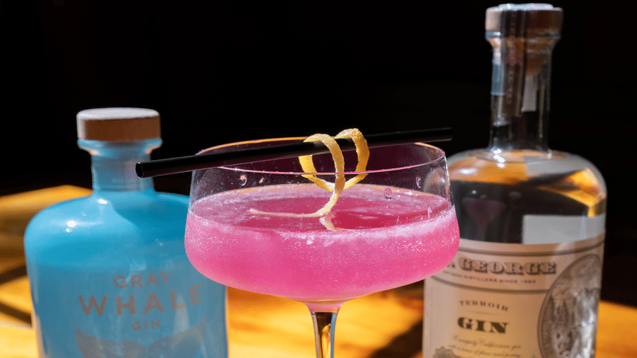 Two vibrant cocktails with lemons and gin bottles on a wooden bar under warm lighting at Narrow Gauge Inn.