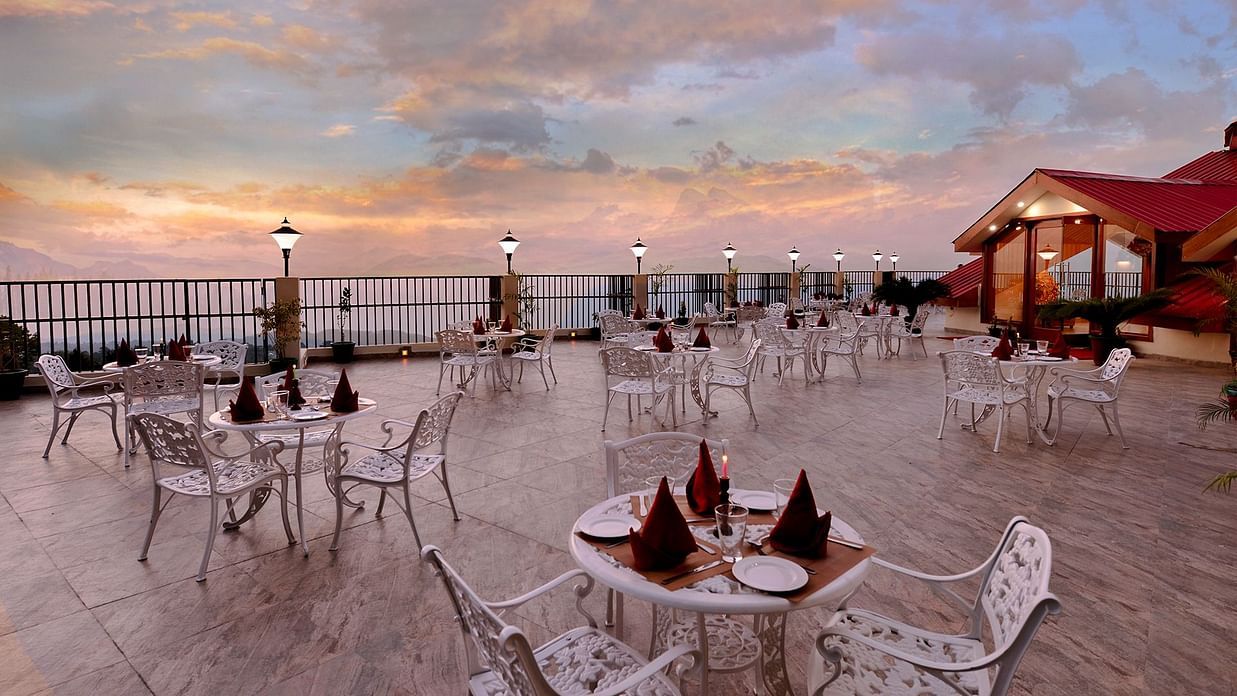 Terrace at JK Clarks Exotica in Dalhousie featuring tables arranged under a colourful evening sky