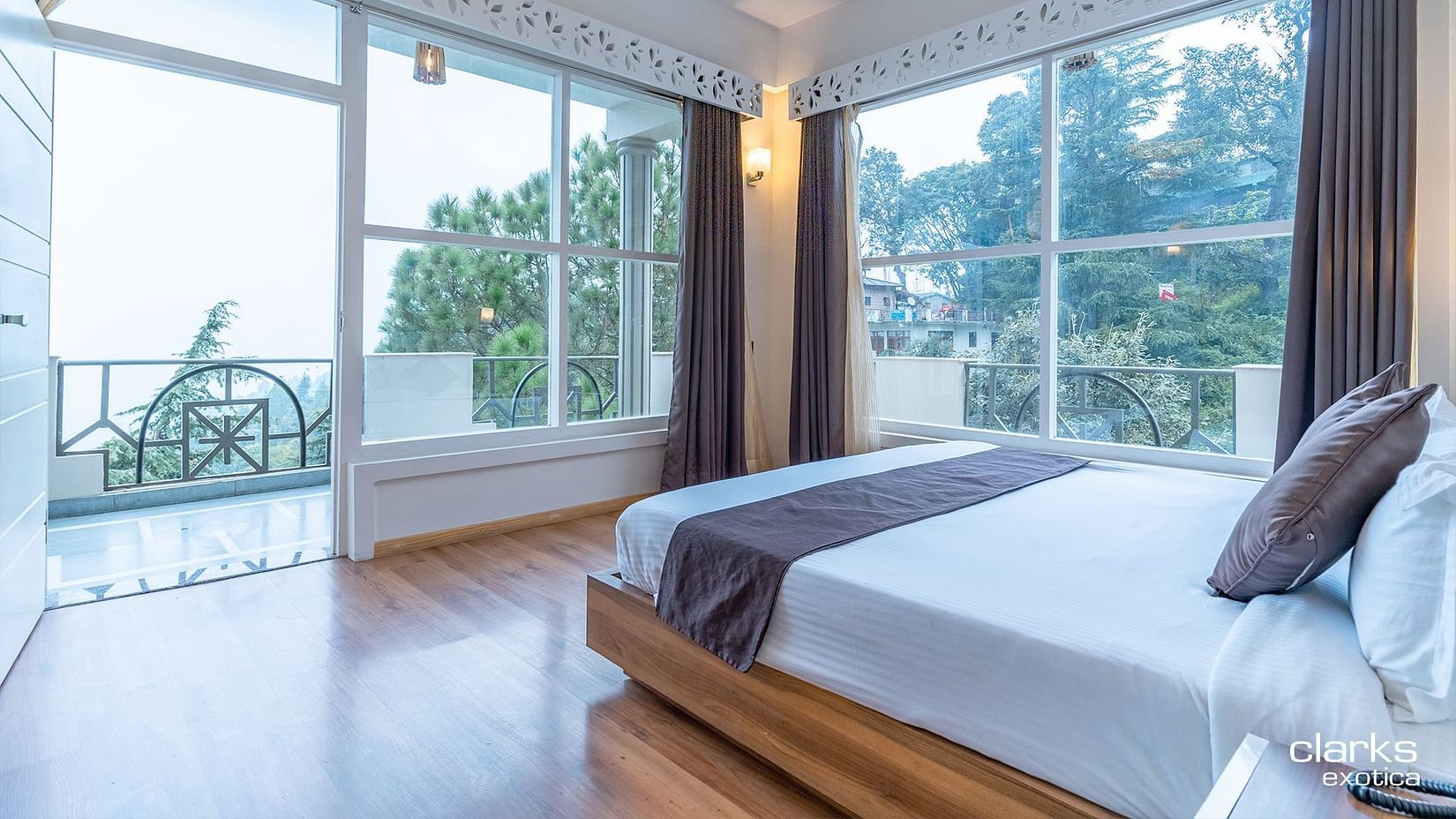 An image of a room featuring plush bed on the wooden floor with a balcony and a huge window next to it