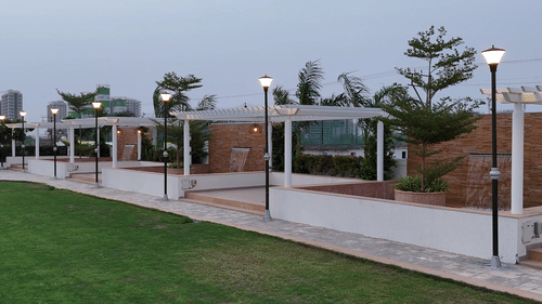 Side view of an expansive lawn with tall halogen lights put up in the perimeter featuring a small water fountain - Pride Resort, Rajkot