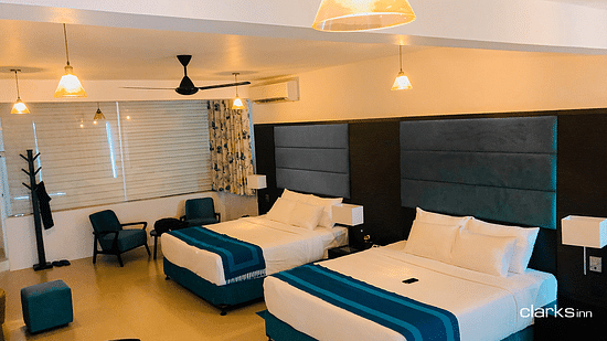 A well-lit room featuring a double bed long with a single bed next to it beside which a couple of couches is placed
