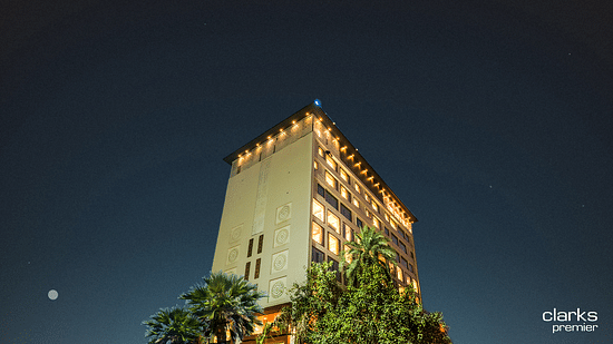 A shot of the top section of the facade of Clarks Premier, Kota in night sky lit up with warm lights and surrounded by trees