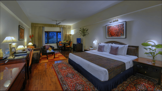 A Junior Suite at The Clarks Varanasi featuring a neatly-made bed, a patterned carpet, wooden furniture and a seating area.