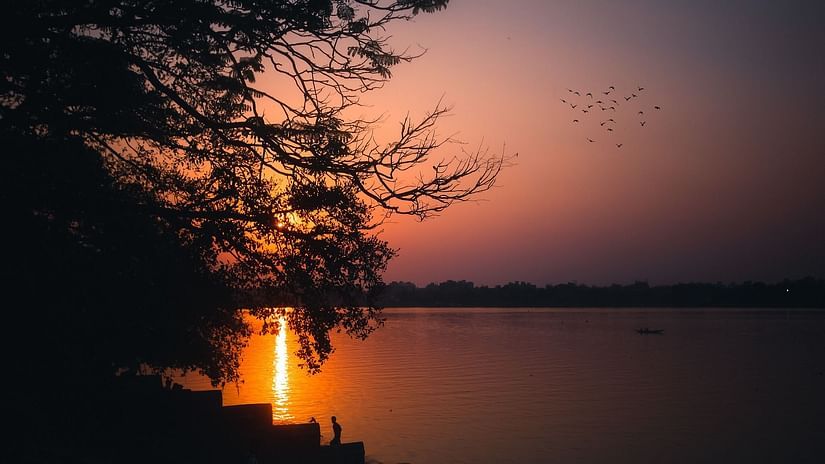 the sun setting on the horizon near a river