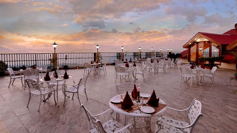 Terrace at JK Clarks Exotica in Dalhousie featuring tables arranged under a colourful evening sky