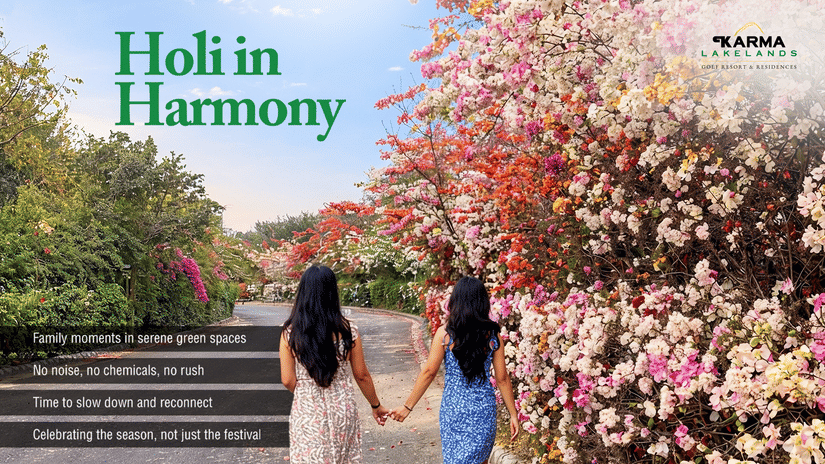 Two people walk hand-in-hand along a flower-lined path at Karma Lakelands, promoting Holi in Harmony, a serene, chemical-free celebration.