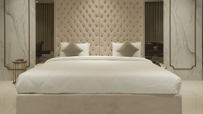 A suite featuring a king size bed with a tufted headboard, two pillows, and marble-style wall panels. - Pride Resort, Rajkot