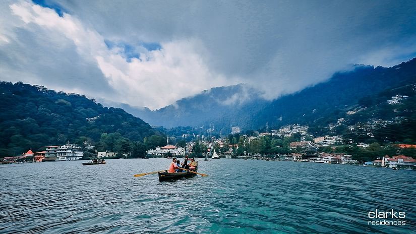 People boating on the Nainital lake amidst mountains and lush greenery under white and blue sky