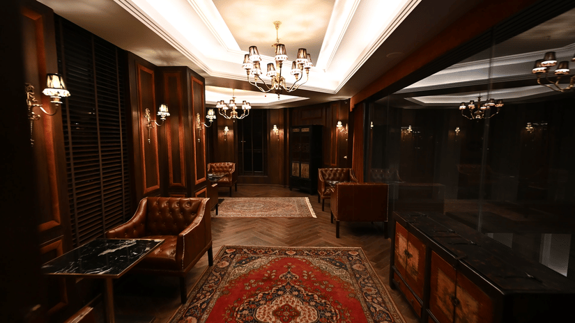 Elegant wood-panelled lounge with leather Chesterfield chairs, crystal chandeliers, and Persian rugs at the Cigar Lounge inside The Manor Wellness & Sports Hotel.