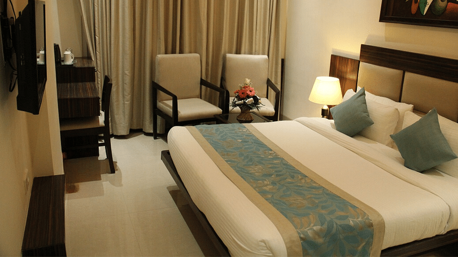 Image of a warm-lit room featuring a plush bed with pillows and cushion and a TV in front of it along with a sitting space next to the bed