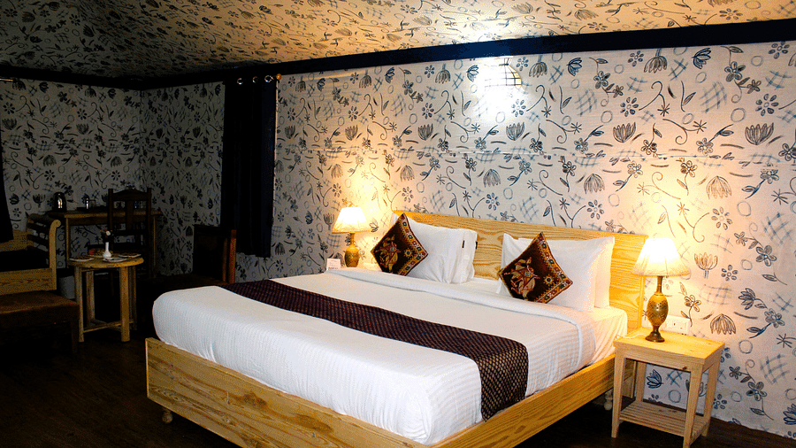 A large bed with two cushions and bedside lamps nearby, with chairs and decorated walls on the room.