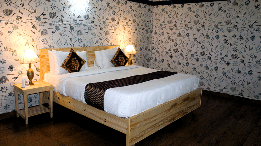 An image showing a large bed with two cushions and bedside lamps nearby, with chairs and decorated walls on the room.