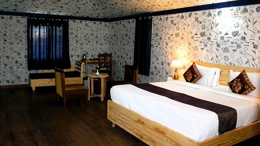 A picture showing a large bed with two cushions and bedside lamps nearby, with chairs and decorated walls on the room.