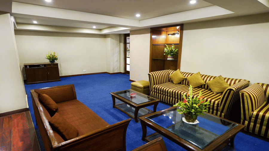 A room with blue carpeting, striped sofas, wooden armchairs, and glass-topped coffee tables | HHI Varanasi