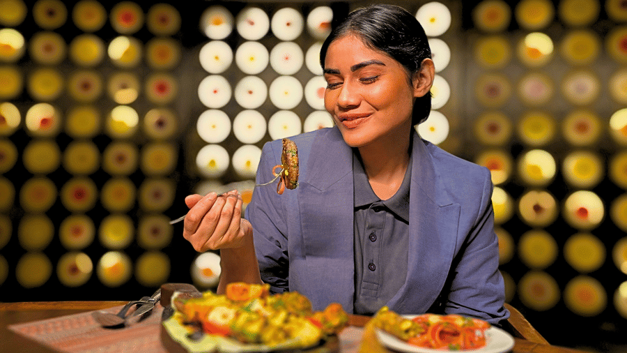 A woman dressed professionally, enjoying BBQ at a restaurant, with a plate of grilled food in front of her.