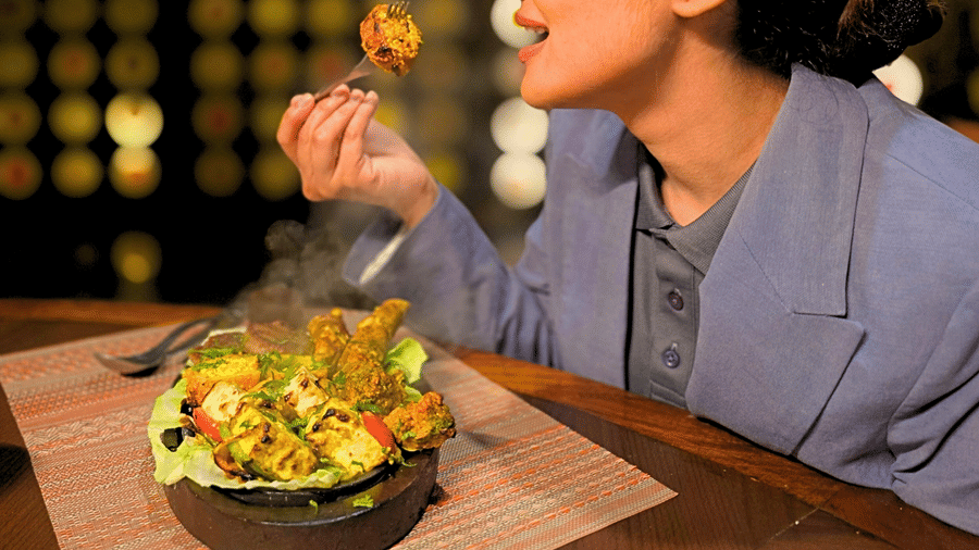 A close side angle of a woman dressed professionally, enjoying BBQ at a restaurant, with a plate of grilled food in front of her.