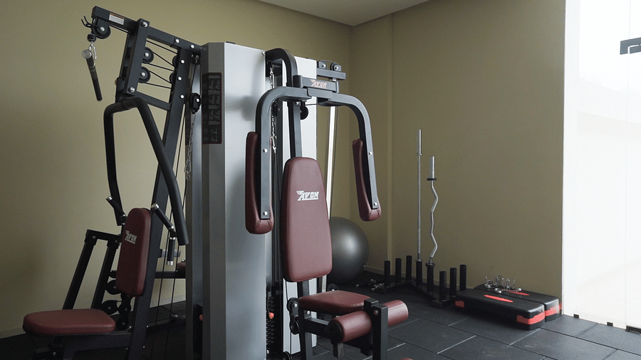 A dedicated gym area at Pride Resort, Rajkot featuring a variety of strength training equipment, including cable machines and weight racks, set against light-coloured walls