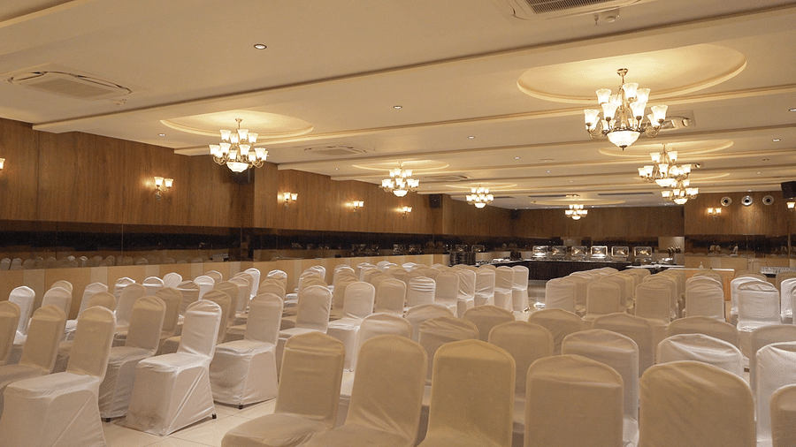 Side view shot of a Imperial hall with central air-conditioning, chandeliers and well arranged seating area - Pride Resort, Rajkot