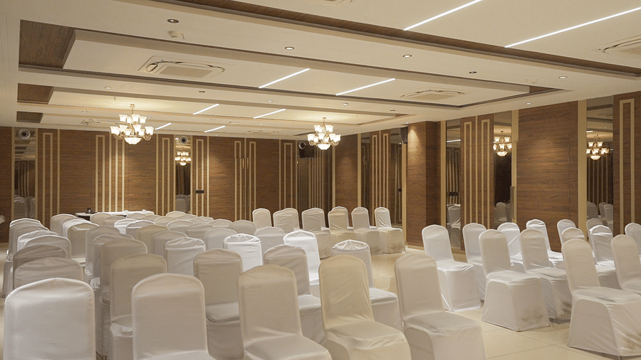 Overview of an expansive banquet hall with white coloured chairs arranged facing towards the stage - Pride Resort, Rajkot