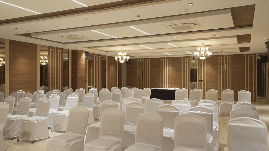 An expansive banquet hall with white coloured chairs arranged facing towards the stage - Pride Resort, Rajkot