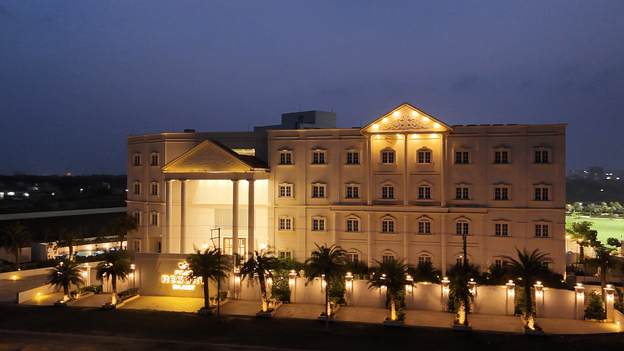 A resort building of Pride Resort Rajkot at twilight, bathed in warm light, highlighting its architectural features and surrounding palm trees against a fading sky.
