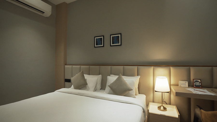  Wide angle shot of Premium Room featuring a comfortable double bed with pillows and cushions arranged over it and night lamp next to it - Pride Resort, Rajkot