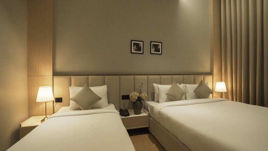 Close up view of Premium Deluxe bedroom with a double and a single bed with bed side lamps lit besides them and paintings hanging on the wall - Pride Resort, Rajkot
