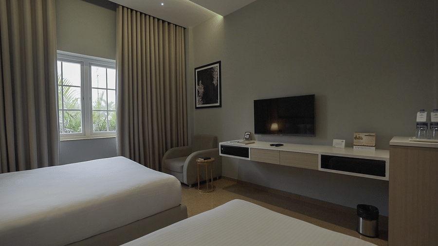 Overview of Premium Deluxe bedroom with a double and a single bed with bed a TV, table and a large window with curtains open - Pride Resort, Rajkot