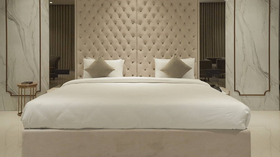 A suite featuring a king size bed with a tufted headboard, two pillows, and marble-style wall panels. - Pride Resort, Rajkot