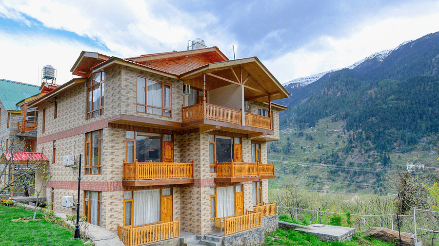 Exterior view of a charming wooden chalet at The Clarks Hotels & Resorts, nestled amidst a scenic mountain landscape.