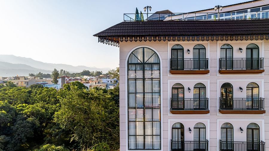Exterior view of a modern hotel building with balconies overlooking a lush green landscape.