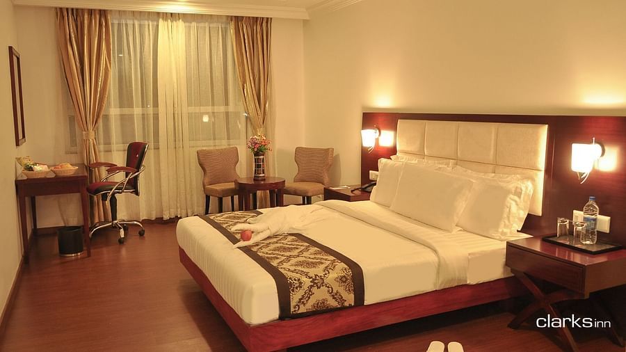 A warm-lit bedroom featuring a plush bed with nighstand and work desk as well as sitting space