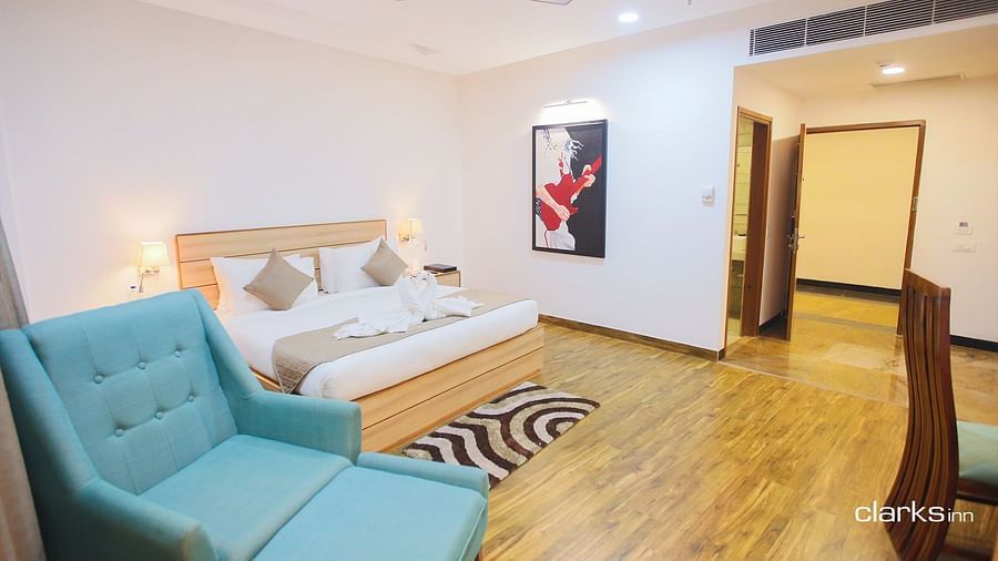 A well-lit room with wooden floor featuring a double bed and a couch next to it 