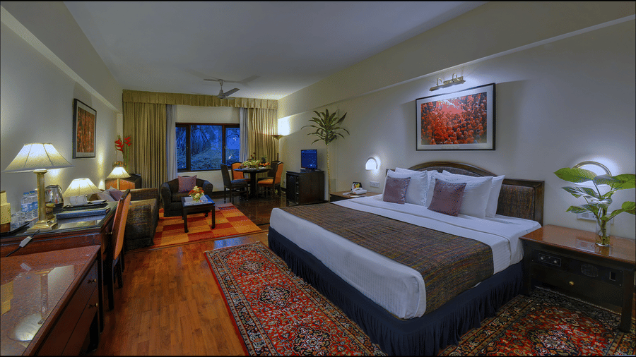 A Junior Suite at The Clarks Varanasi featuring a neatly-made bed, a patterned carpet, wooden furniture and a seating area.