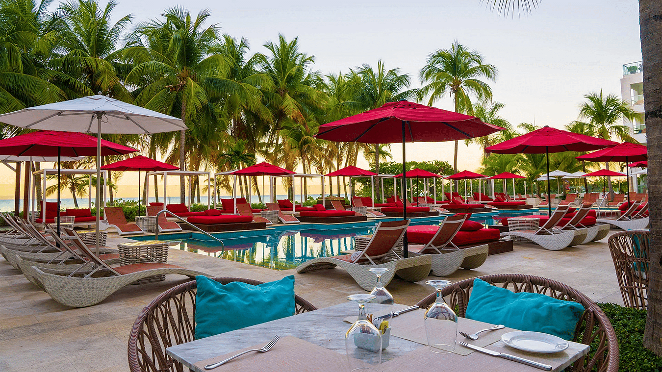An image of a pool seen during a sunset with sun loungers and a lush green backdrop - S Hotels, Jamaica