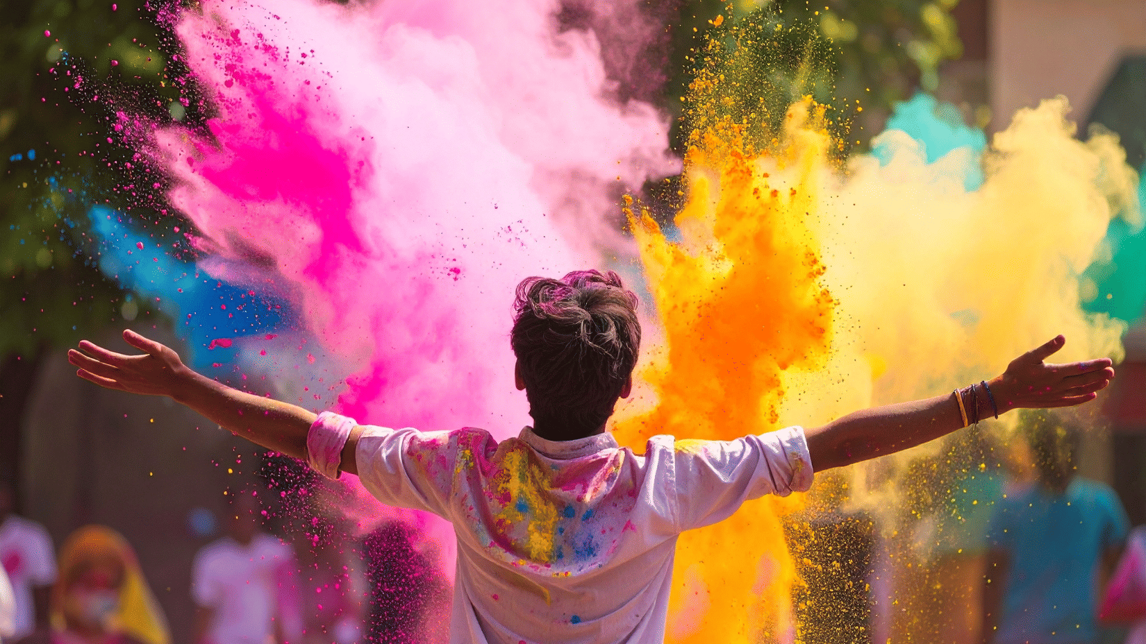 A joyful Holi celebration with vibrant clouds of pink, yellow and blue colours as a person stands with arms open, capturing the festive spirit and energy of the festival.