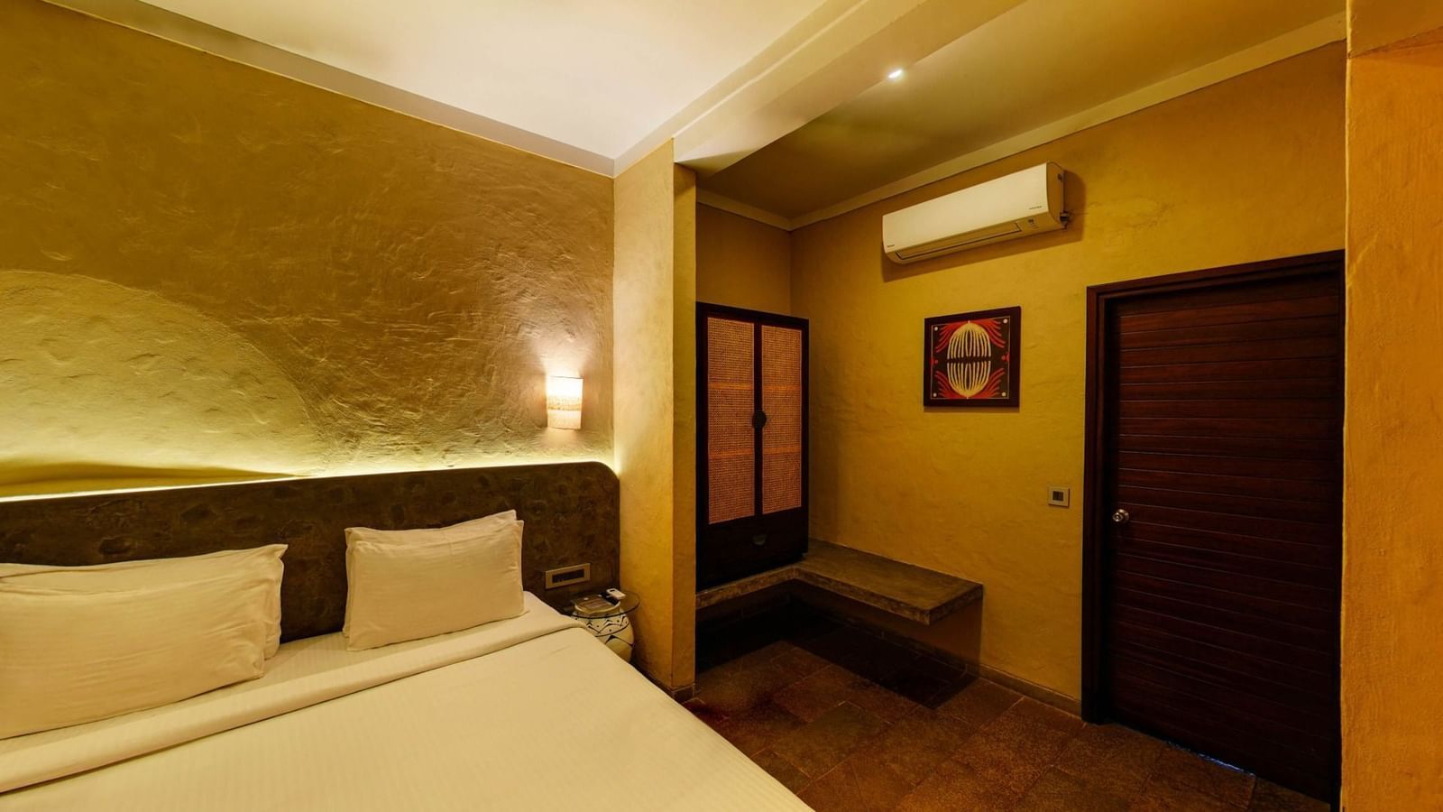 Room with partially visible bed, cushioned headboard, framed artwork on the wall, and wooden wardrobe at Fireflies Resorts, Kabini.
