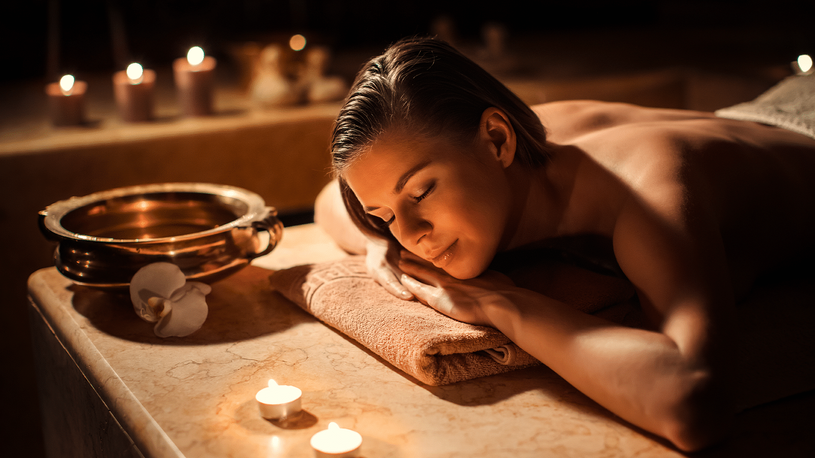 Woman relaxing during a spa treatment surrounded by candles, enjoying a moment of calm