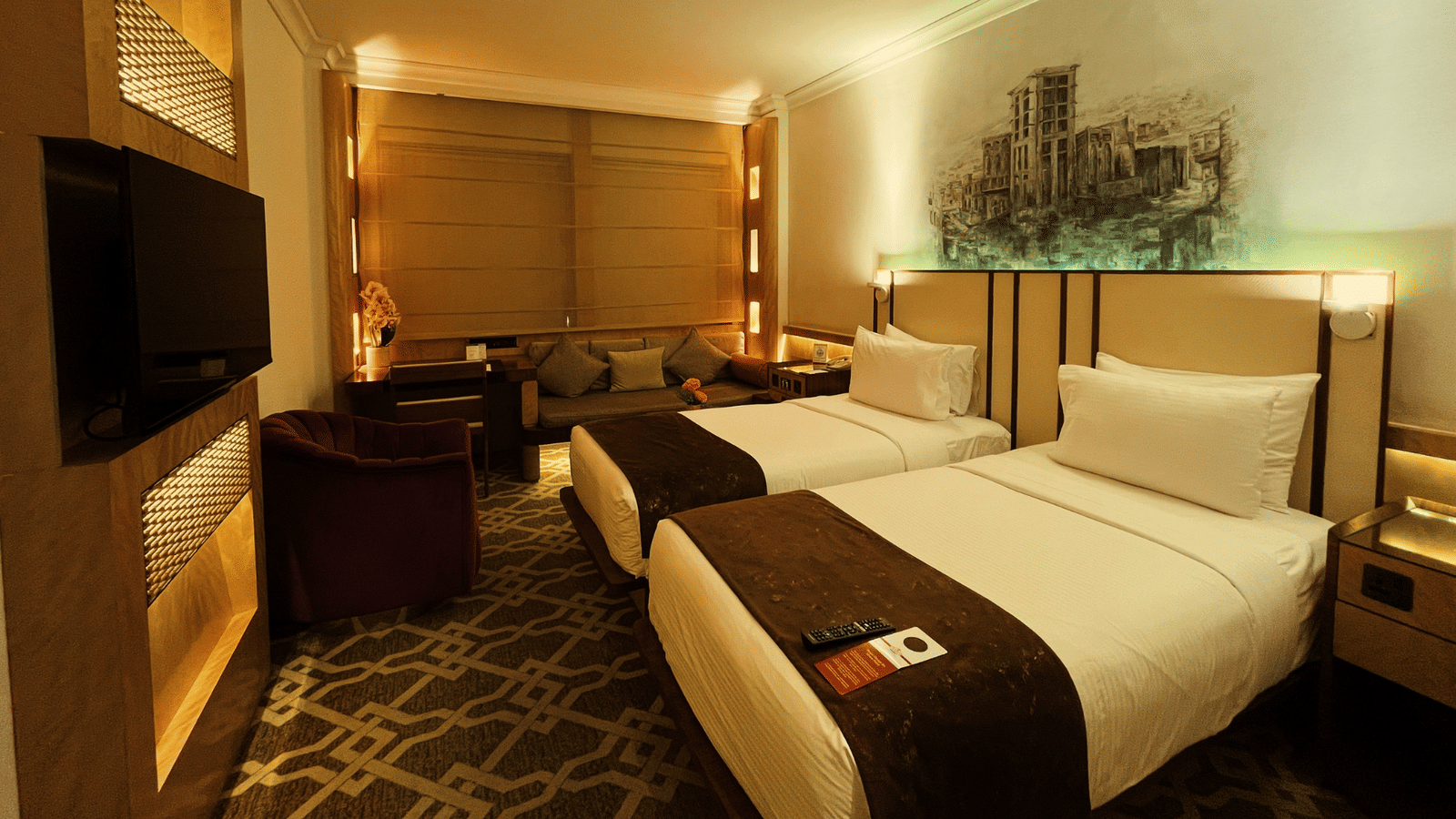 Wide shot of two twin beds, a television screen, and an armchair in a room at Marco Polo Hotel.