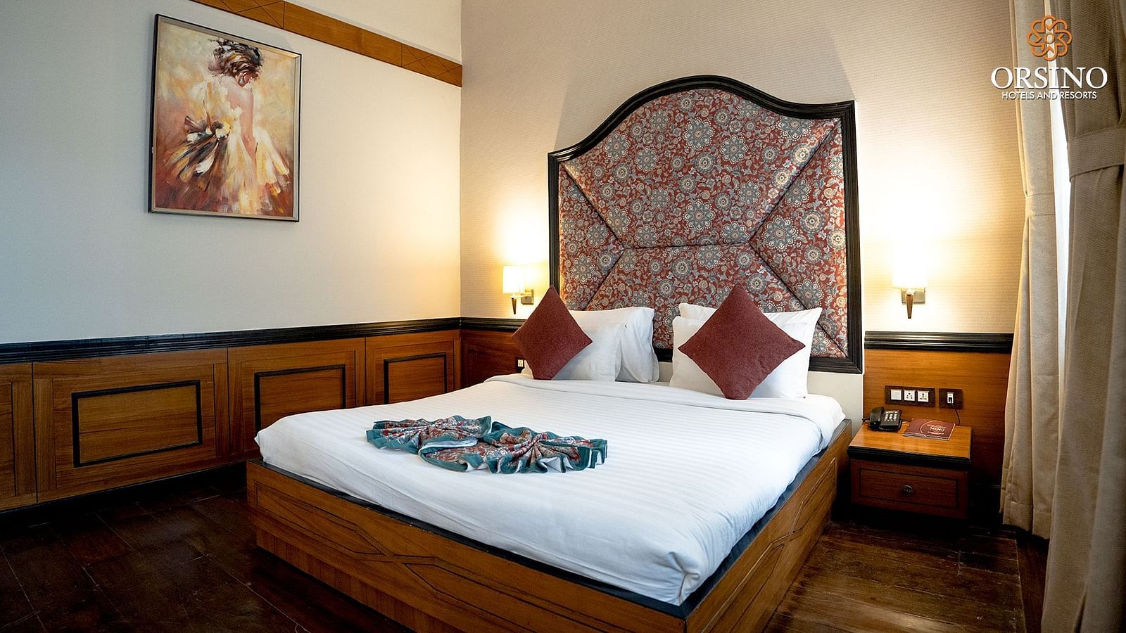 A room at Orsino Spa Resort with a bed featuring a prominent, patterned headboard and a white duvet with a colourful throw.