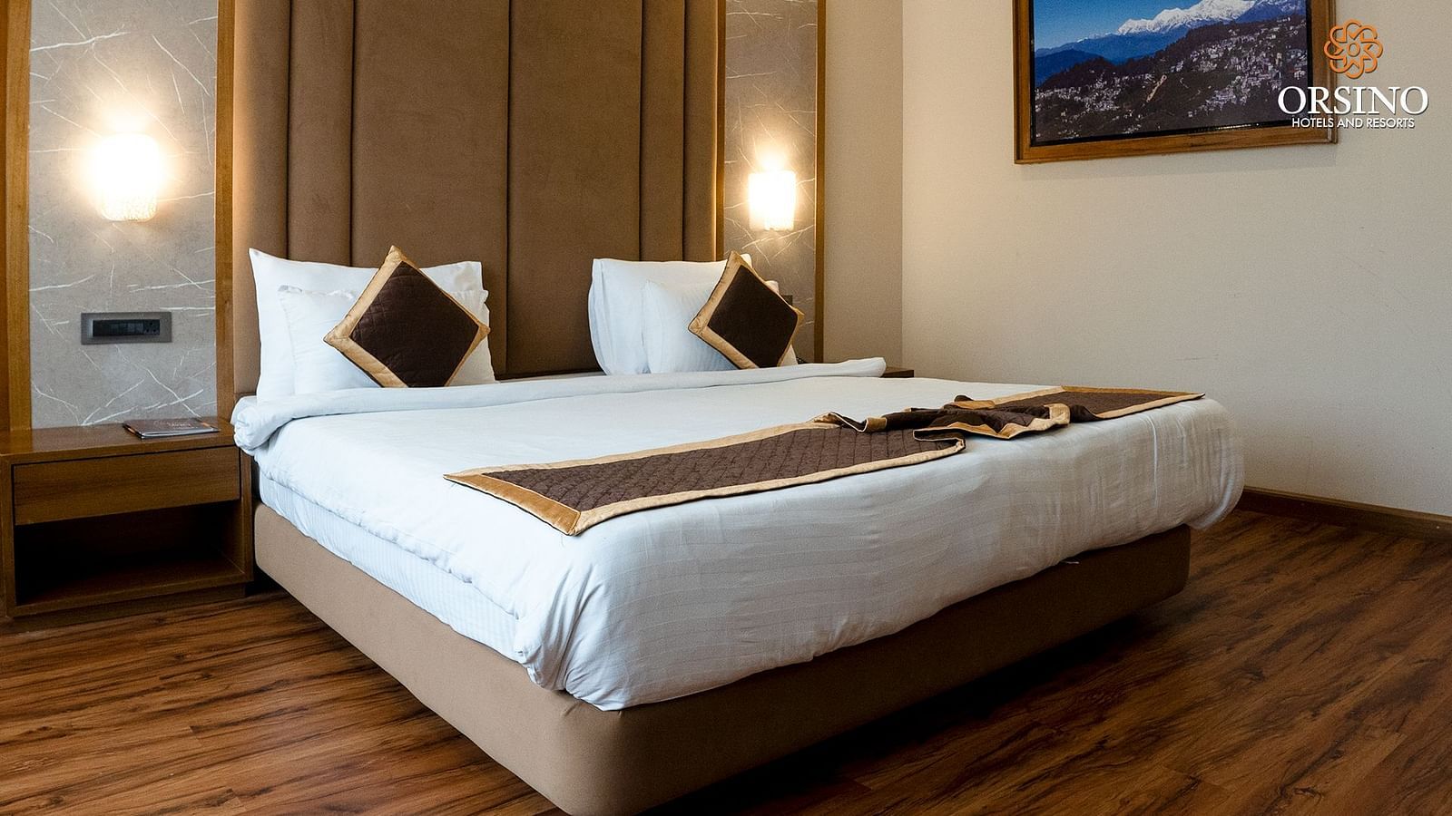 A room at Orsino Spa Resort with a large bed, a cushioned headboard, and bedside lighting, with artwork on the wall.