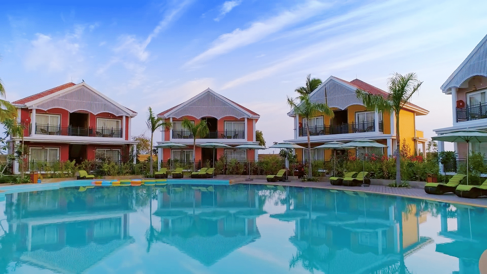 Scenic view of Swosti Chilika Resort featuring a luxurious pool and vibrant cottages under a clear blue sky
