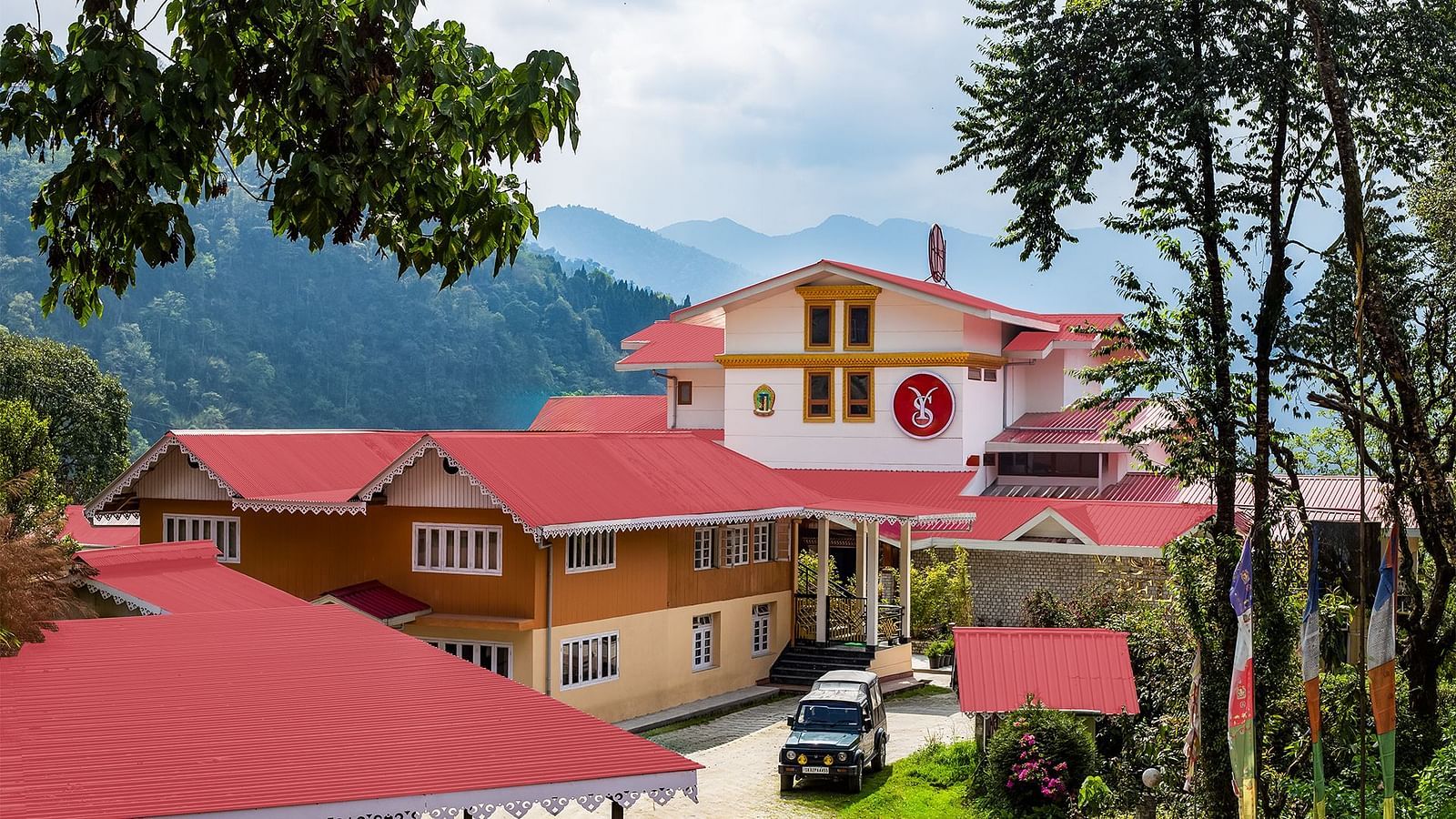 Charming hillside buildings with red rooftops set against a backdrop of lush green mountains under a partly cloudy sky - Yashshree Pelling Chekhim Retreat.