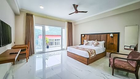  A spacious room at Yashshree Resort & Spa Kalimpong features a large bed, a desk with a wall-mounted TV, an armchair, and a wide glass door leading to an outdoor area.