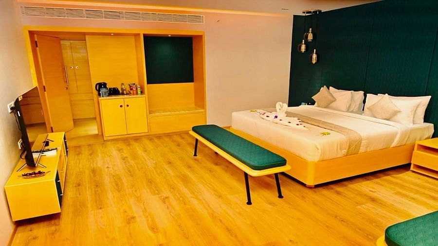 A Presedential Suite featuring a King size bed with white linens and decorative swans, a green accent wall, yellow furniture, and hardwood floors. - Dhanalakshmi Srinivasan Hotels, Perambalur
