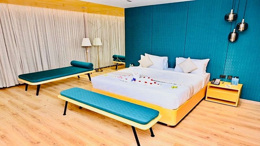 Close up view of a Presedential Suite featuring a King size bed with white linens and decorative swans, a green accent wall, yellow furniture, and hardwood floors - Dhanalakshmi Srinivasan Hotels, Perambalur